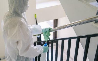 A person wearing a mask, gloves and a safety suit cleans and disinfects a doorway of a community flat in the face of a virus pandemic, protected safety equipment so as not to be infected